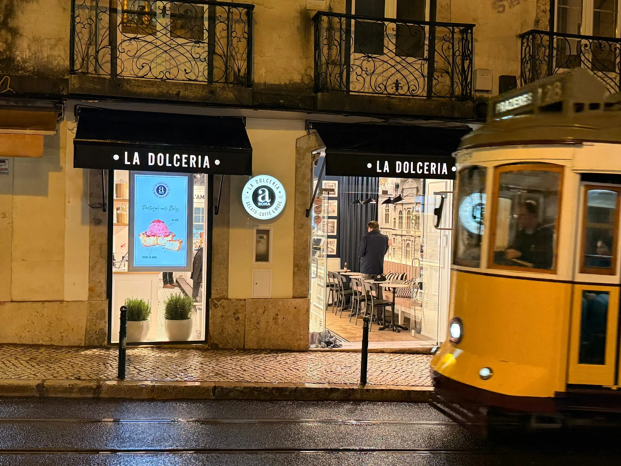 Fachada da La Dolceria aROMA na Rua do Loreto, à noite, com o elétrico 28 a passar