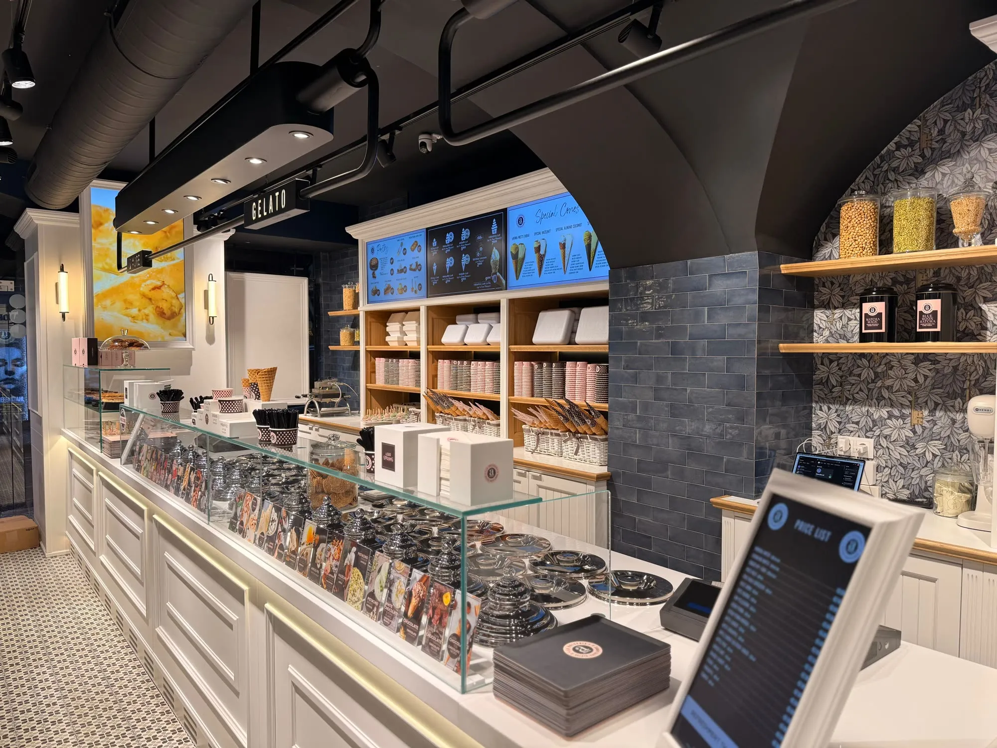 Zona de gelataria com o arco em azulejo escuro, prateleiras em madeira e vitrina de gelados