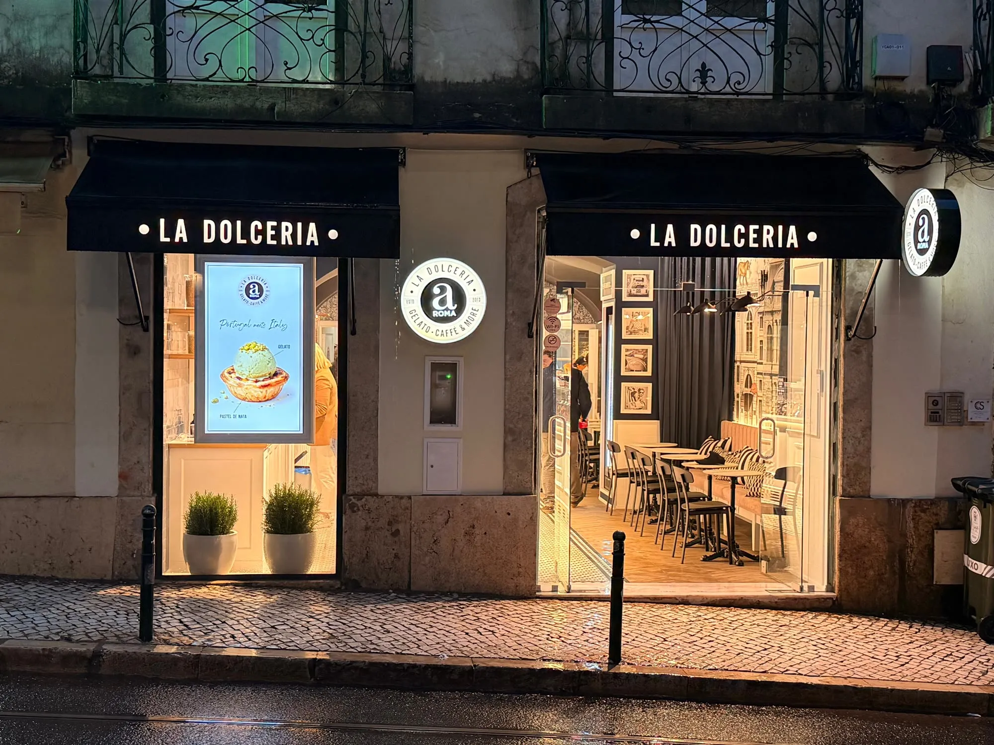 Montra da La Dolceria aROMA iluminada à noite, com as portas abertas para a rua