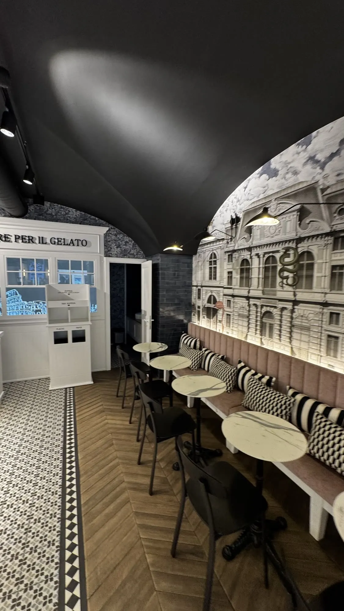 Sala de clientes com bancada corrida, mesas em mármore e o mural de fachadas em papel de parede