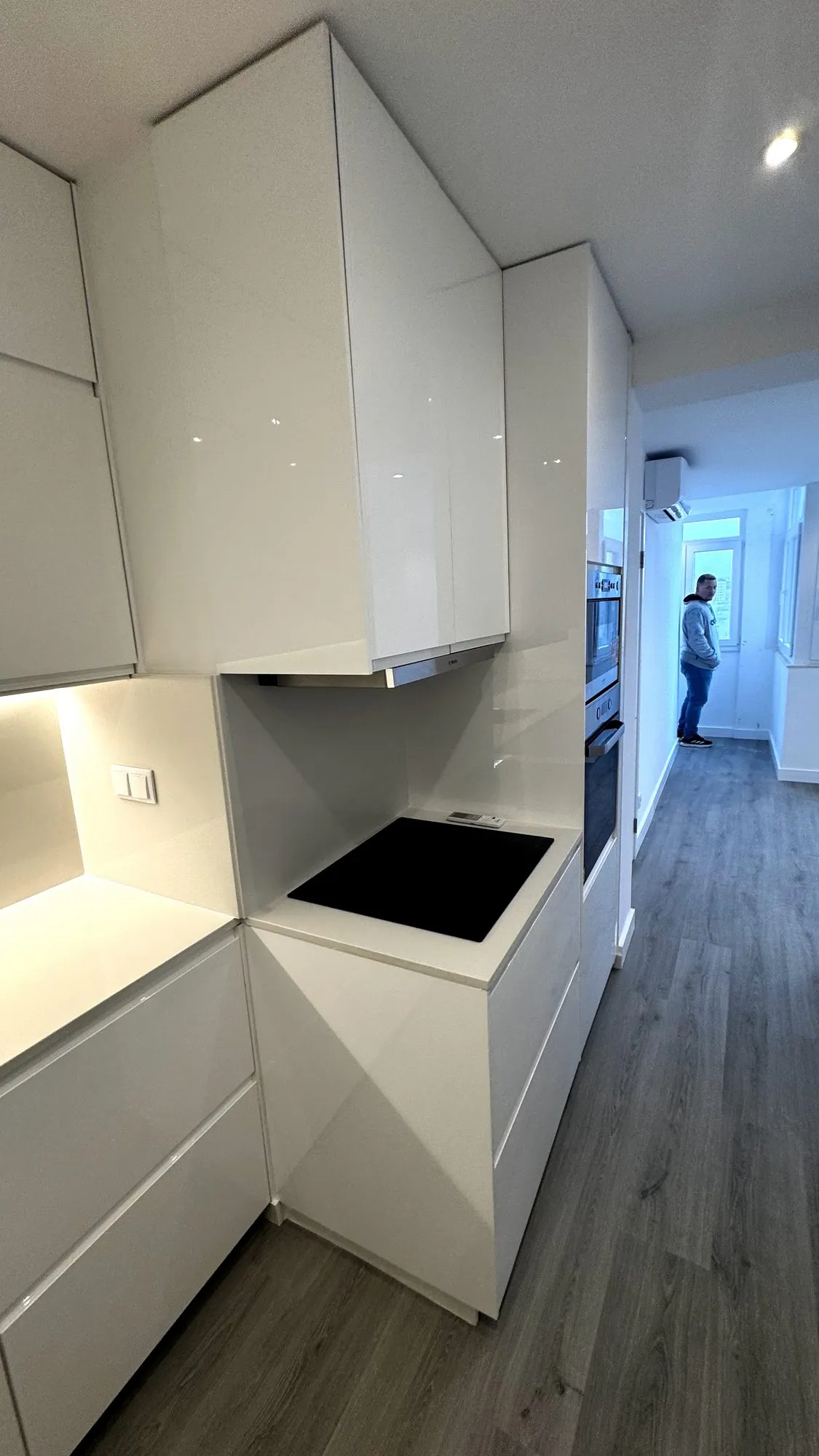 Zona da cozinha com exaustor e forno de encastrar, e o corredor de acesso ao quarto ao fundo