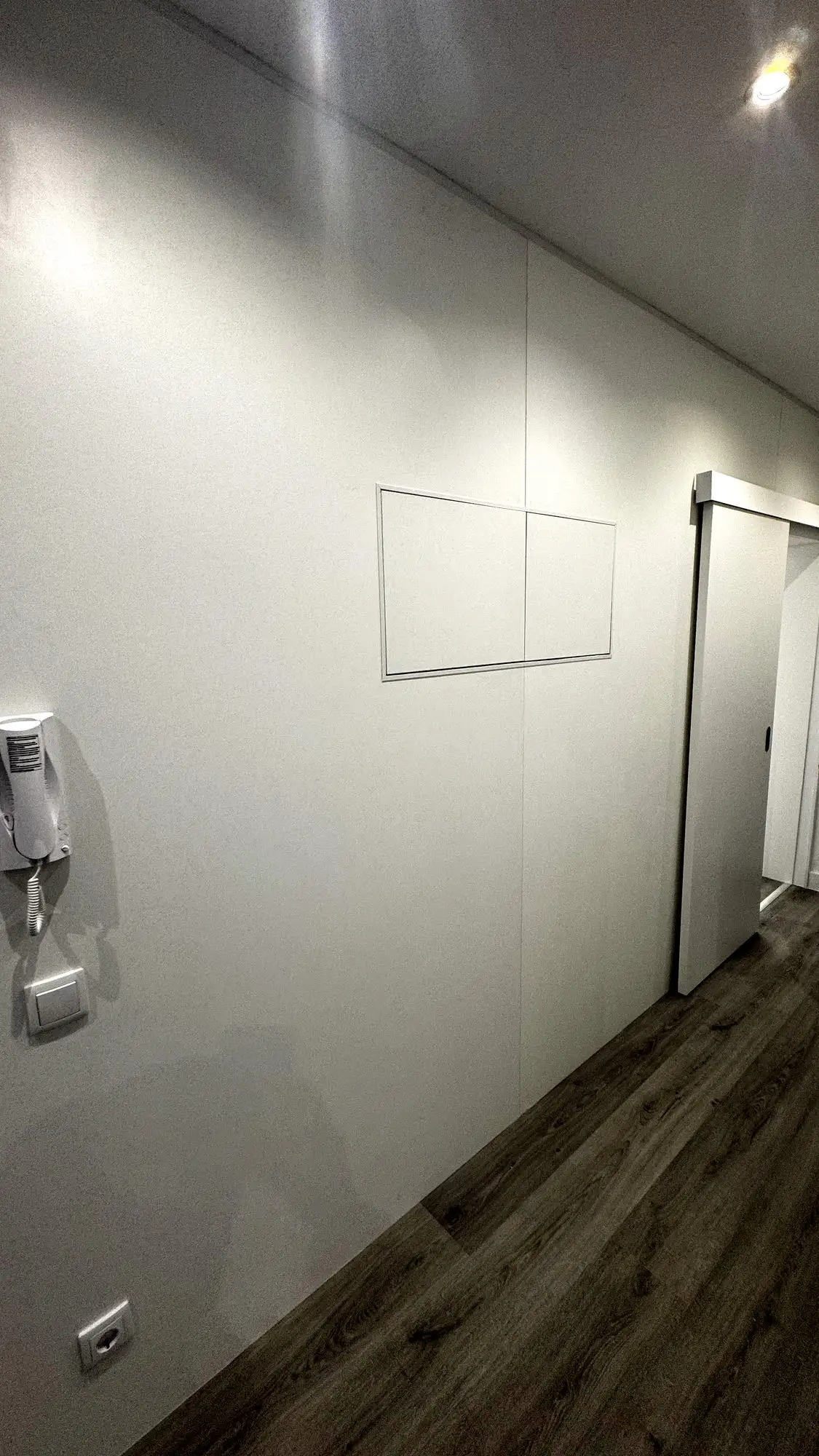 Corredor com porta de correr embutida e alçapão de acesso técnico, em painel liso