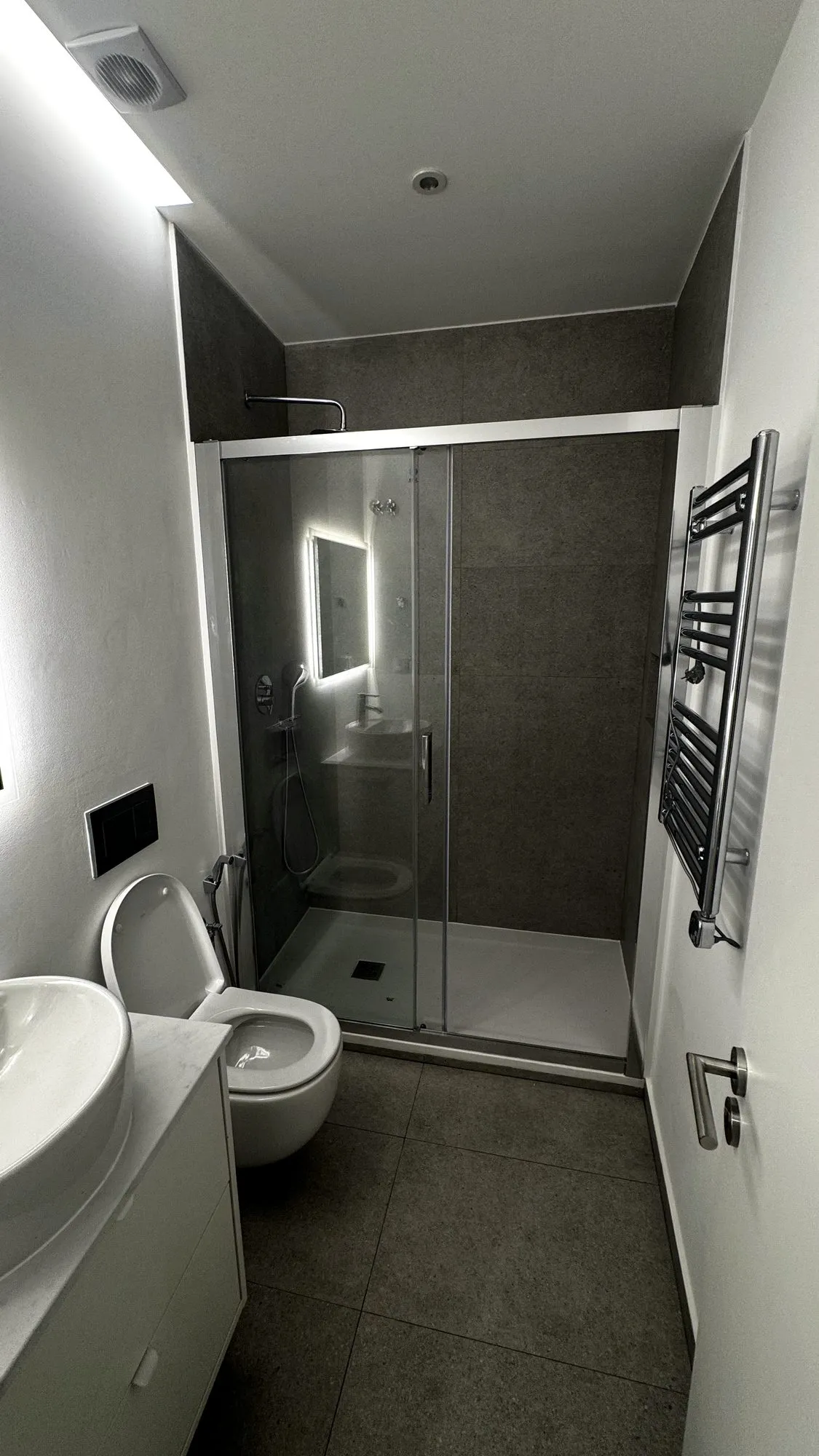 Segunda casa de banho, com base de duche, sanita suspensa e revestimento cerâmico cinzento