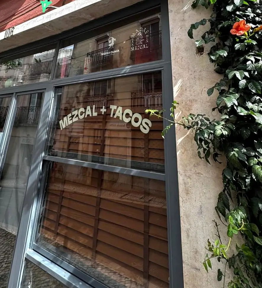Fachada da Bodega Chafa com as letras 'Mezcal + Tacos' no vidro e uma trepadeira