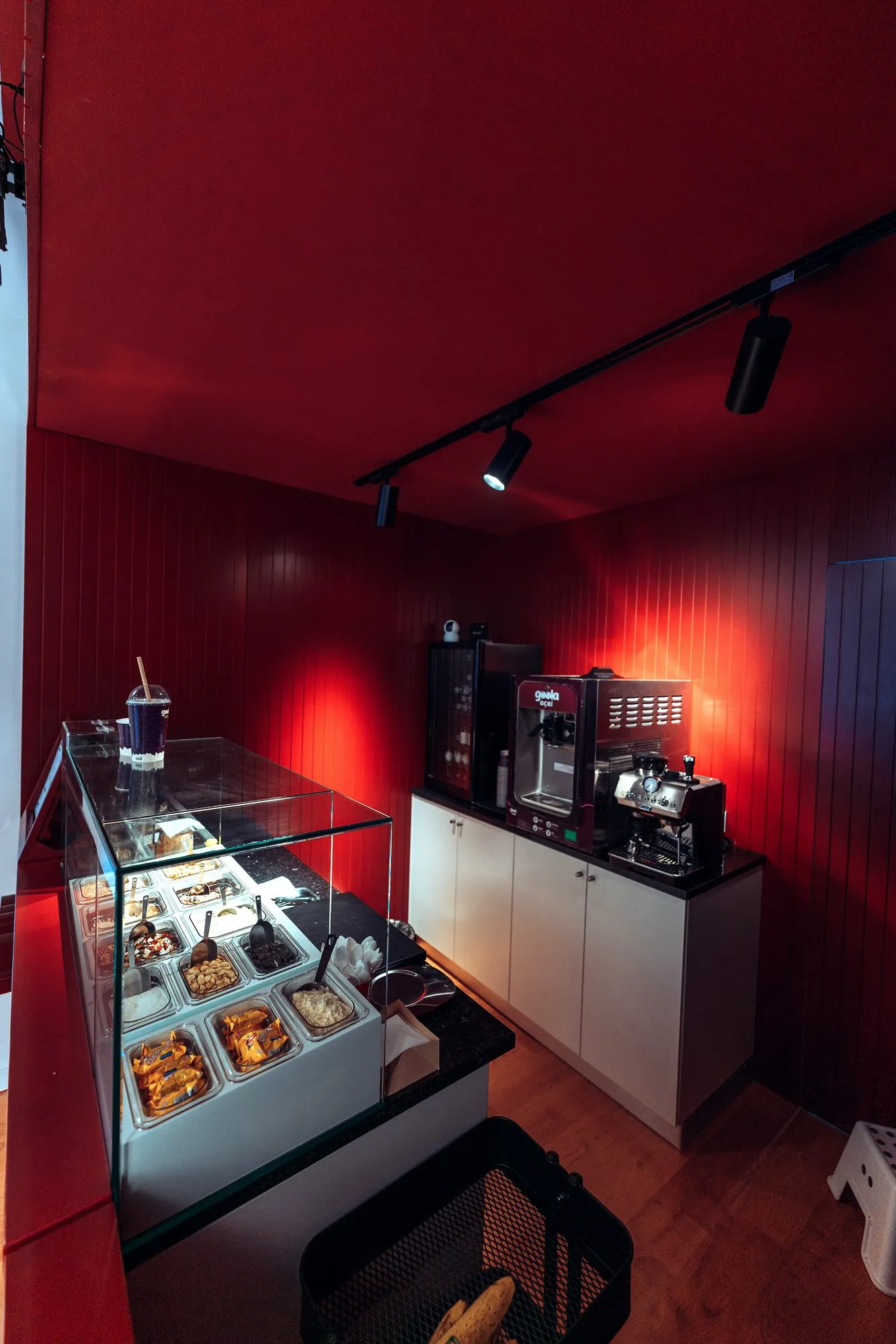Vitrina de bolos e máquina de café sobre os armários de serviço, contra a parede vermelha em régua